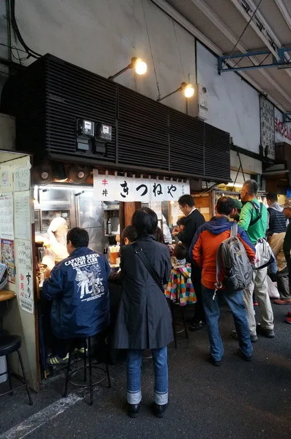 築地場外の軒下、きつねやの店先で立ち食いする客と煮込み鍋
